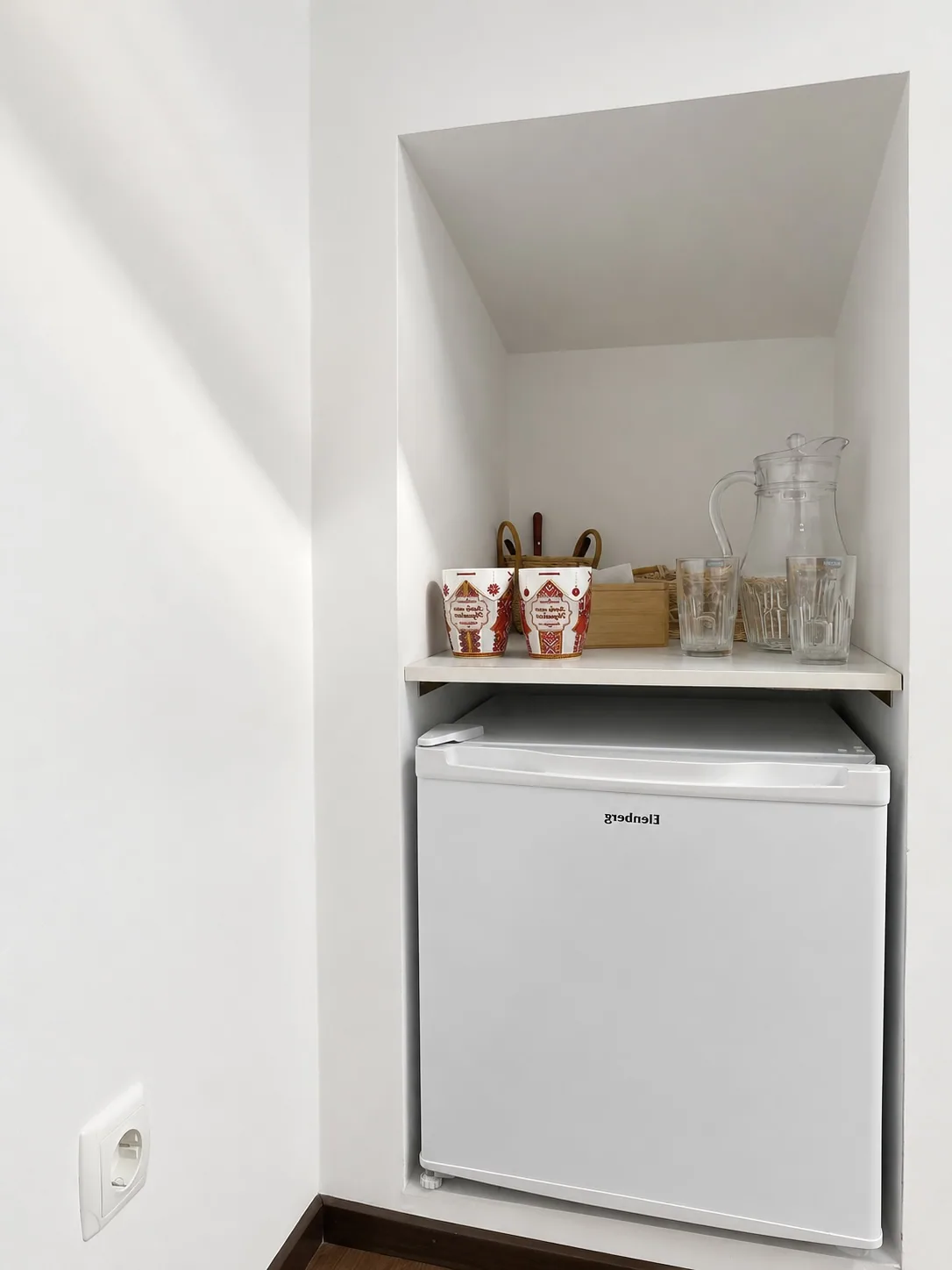 Fridge and a shelf with mugs in the air-conditioned attic room