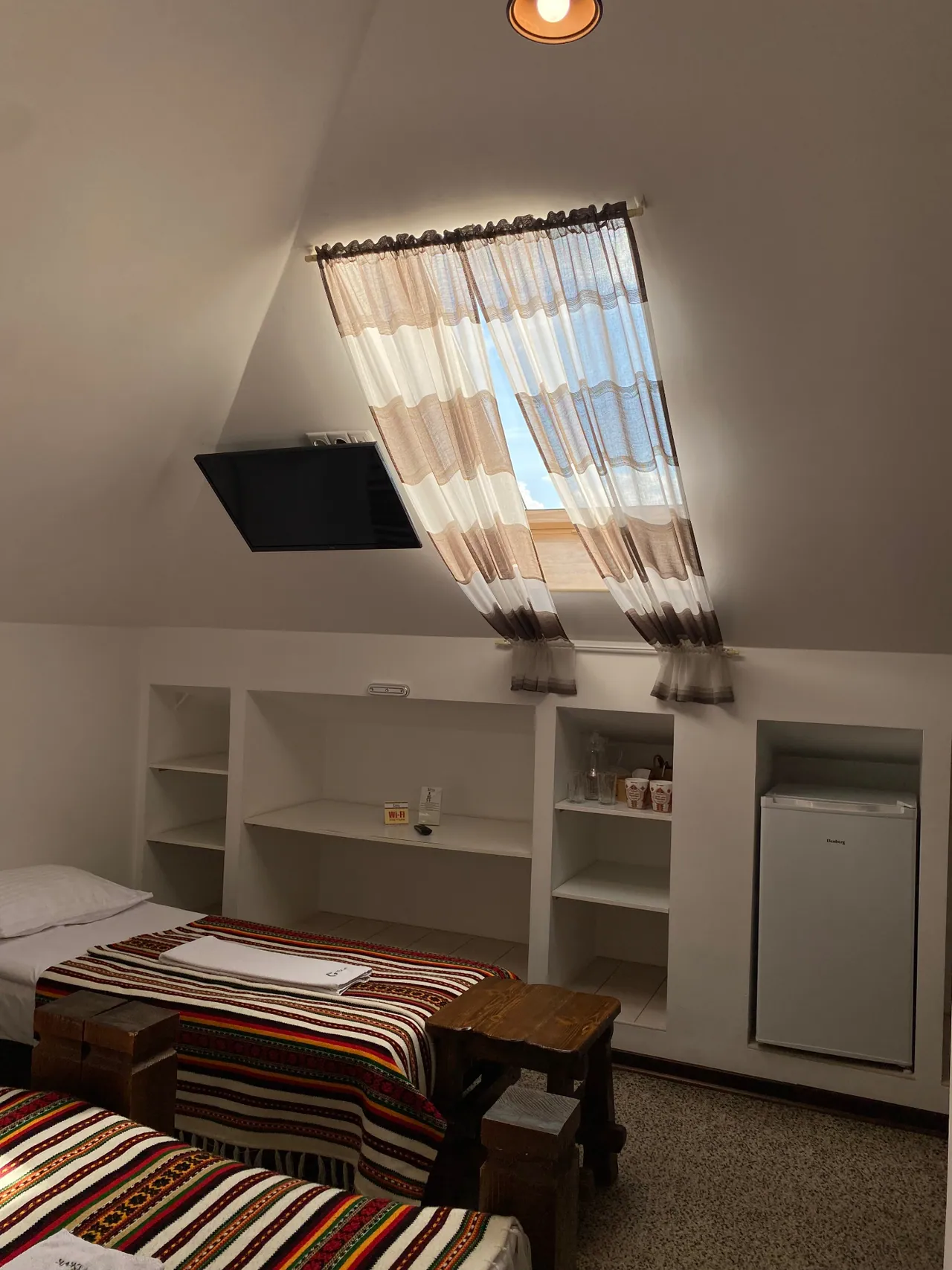 Attic room with a window, shelves, TV and fridge